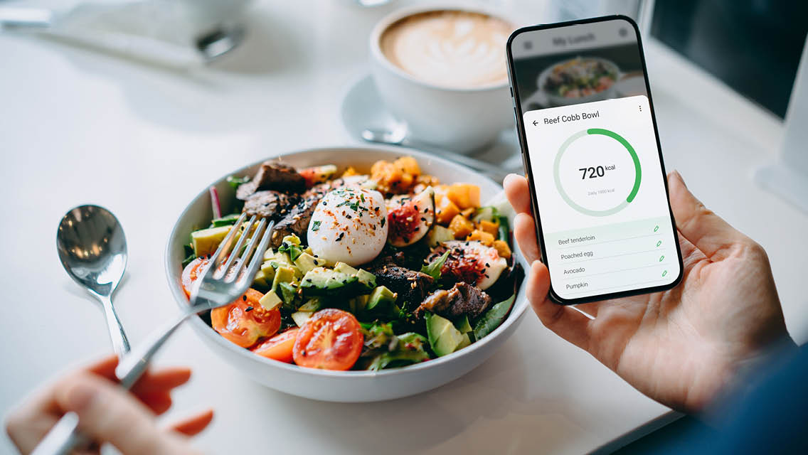 a person prepares to a eat salad with their phone open to a calorie counting app