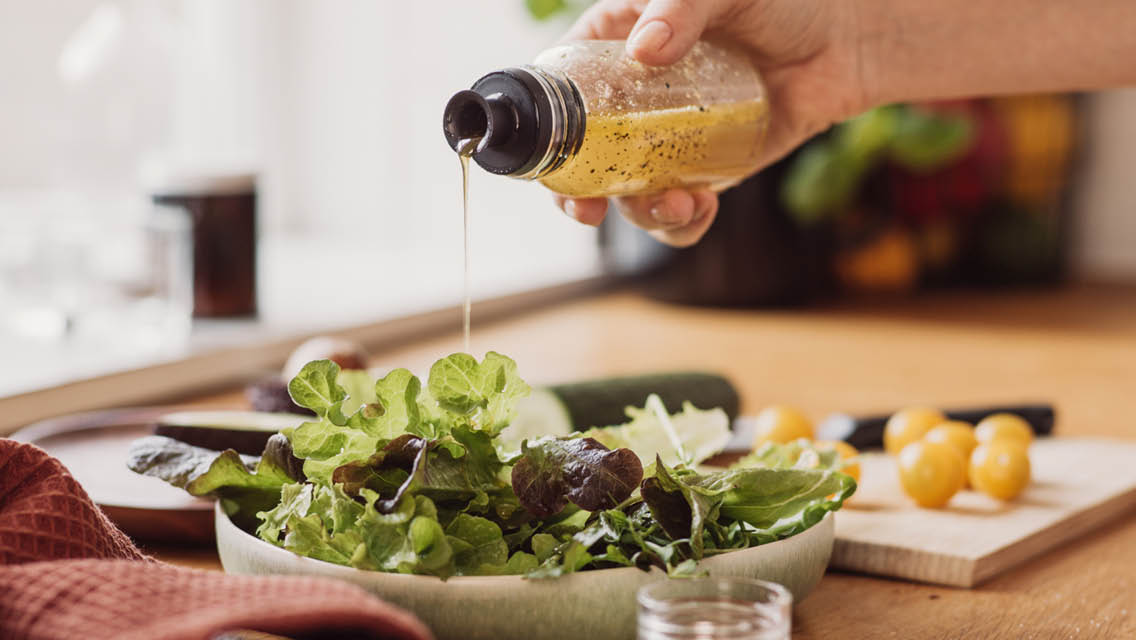 a person drizzles homemade dressing on a salad