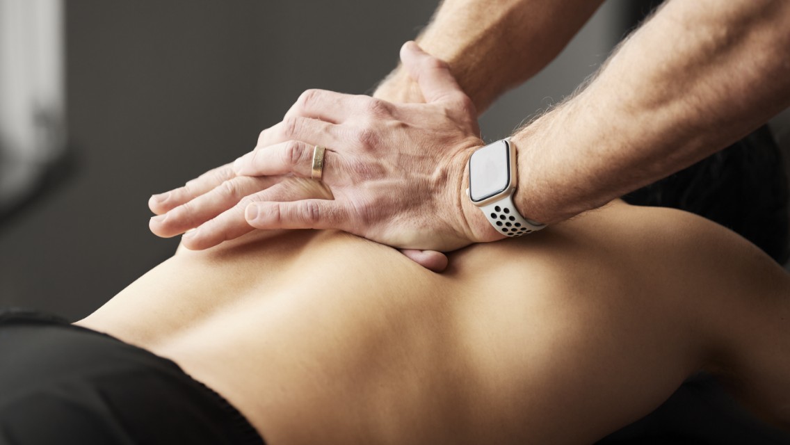 A chiropractor placing two hands on a patient's back