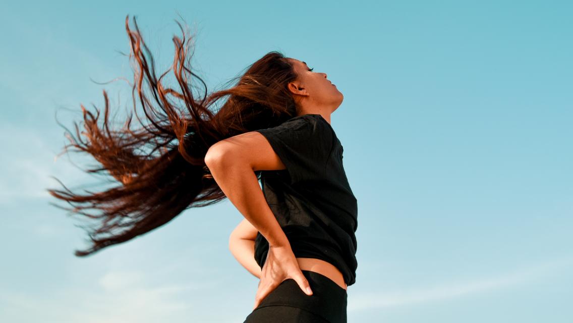 A woman outside flipping her long hair in the wind.