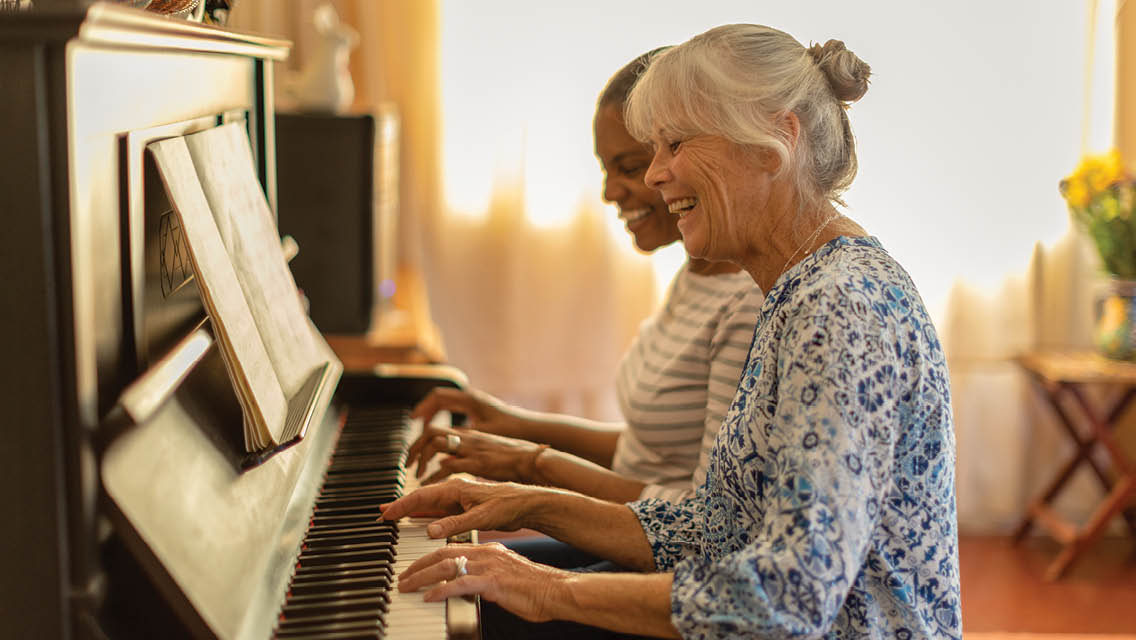 two women play piano while laughing