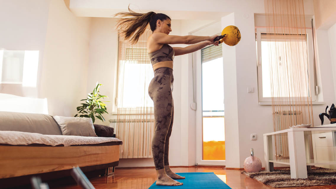 a woman swings a kettlebell in her living room