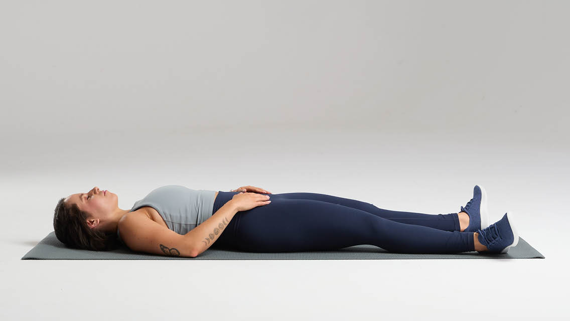 a woman lays on the floor with her hands resting on her pelvis