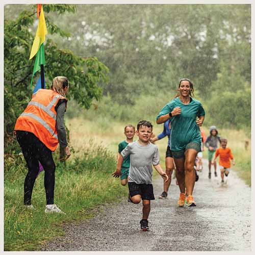 kids and a mom run through the rain during a mud run race