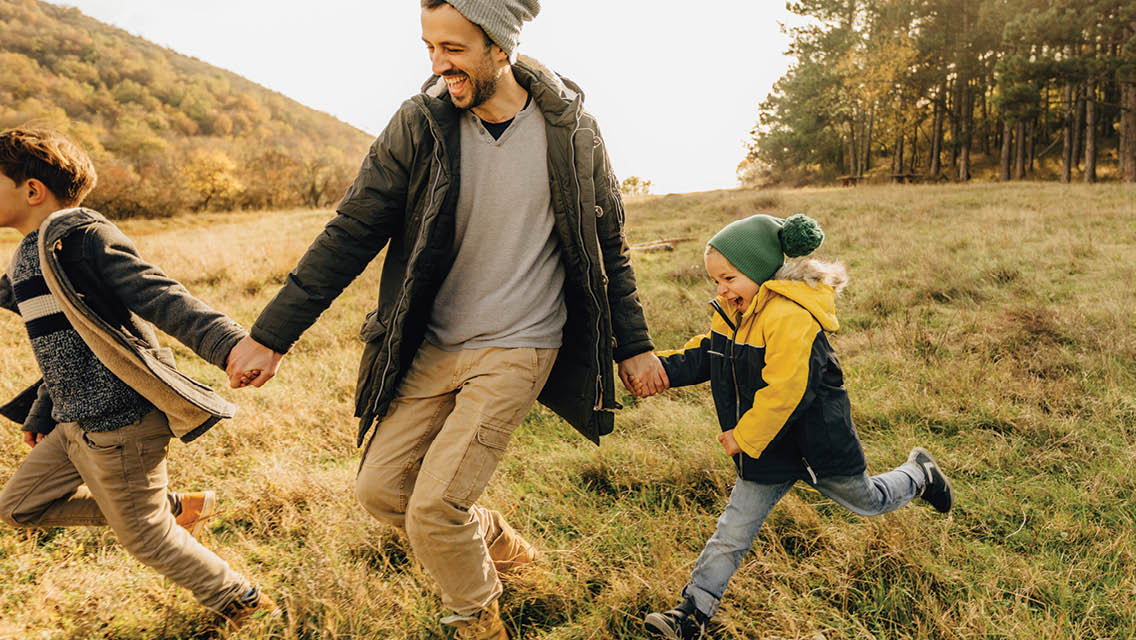 a dad runs through a field with his kids