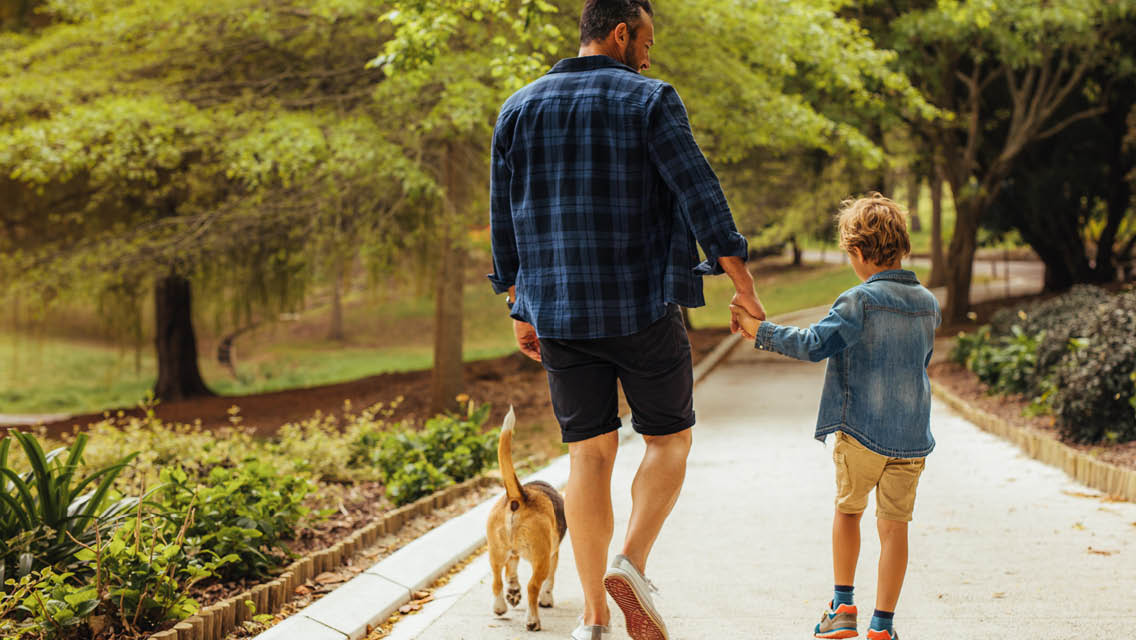 a father and son walk their dog in a park