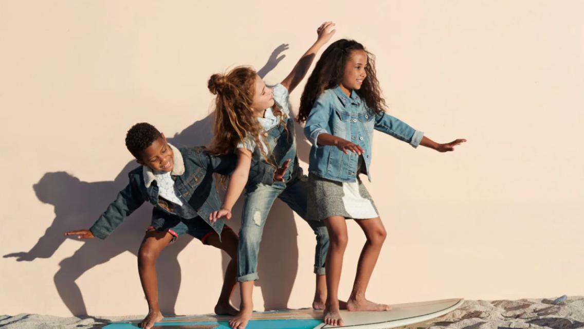 Three kids on a surfboard on the sand.