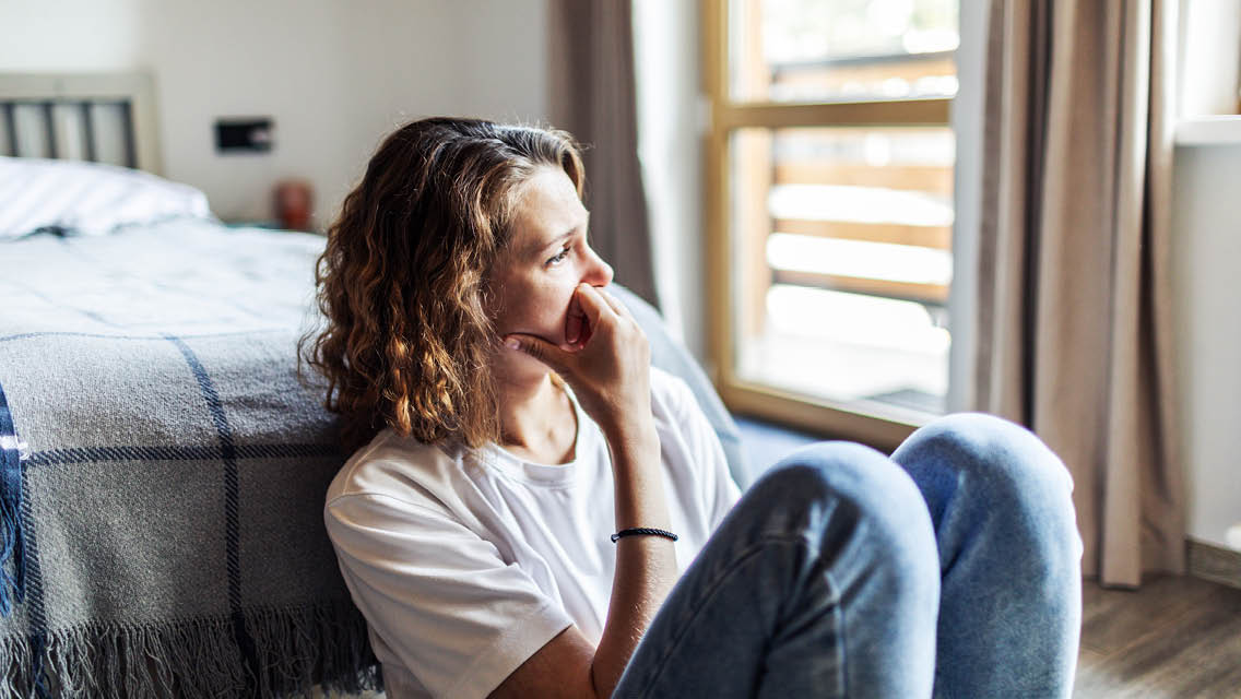 a woman sits on the floor in her room looking out the window