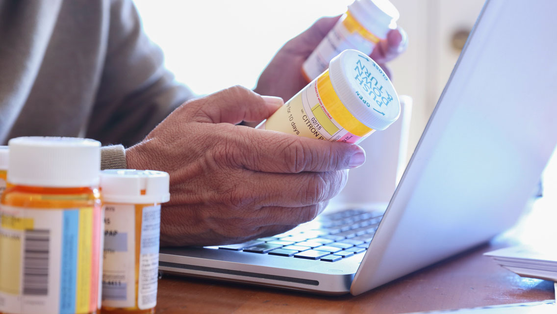 A person compares two bottles of pills as they sit at a laptop.