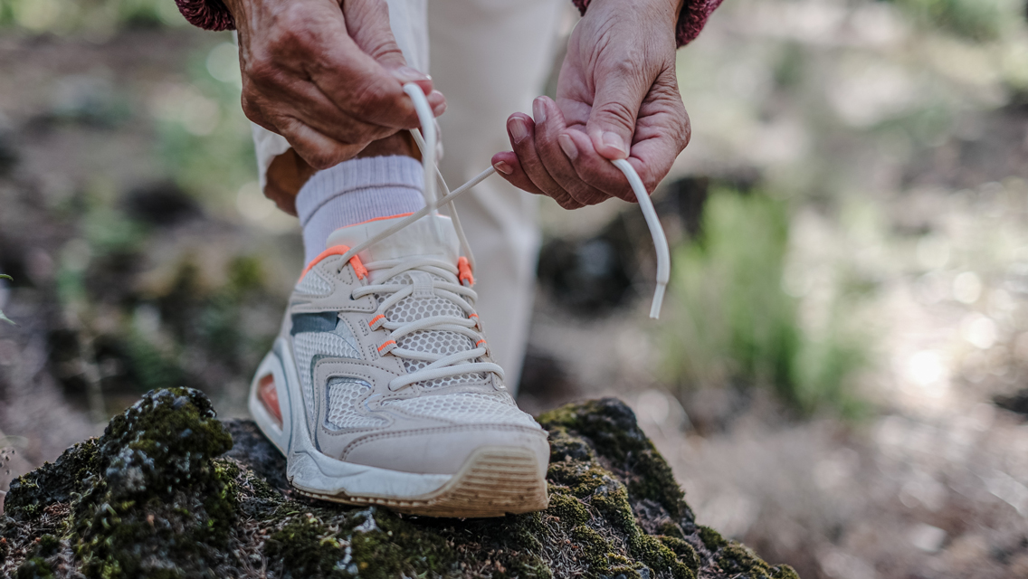 a senior woman ties her tennis shoe in a nature setting