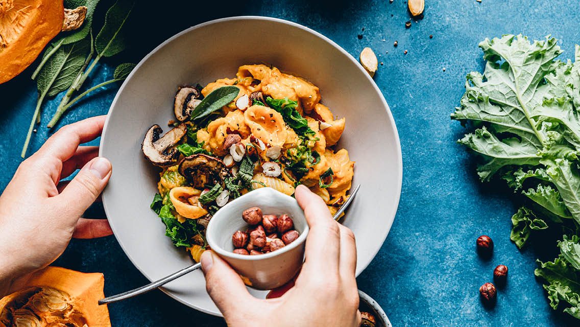 a bowl of pasta with mushrooms and someone adding nuts to it