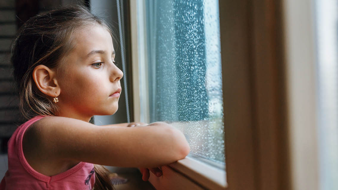 a young girl looks out a rainy window