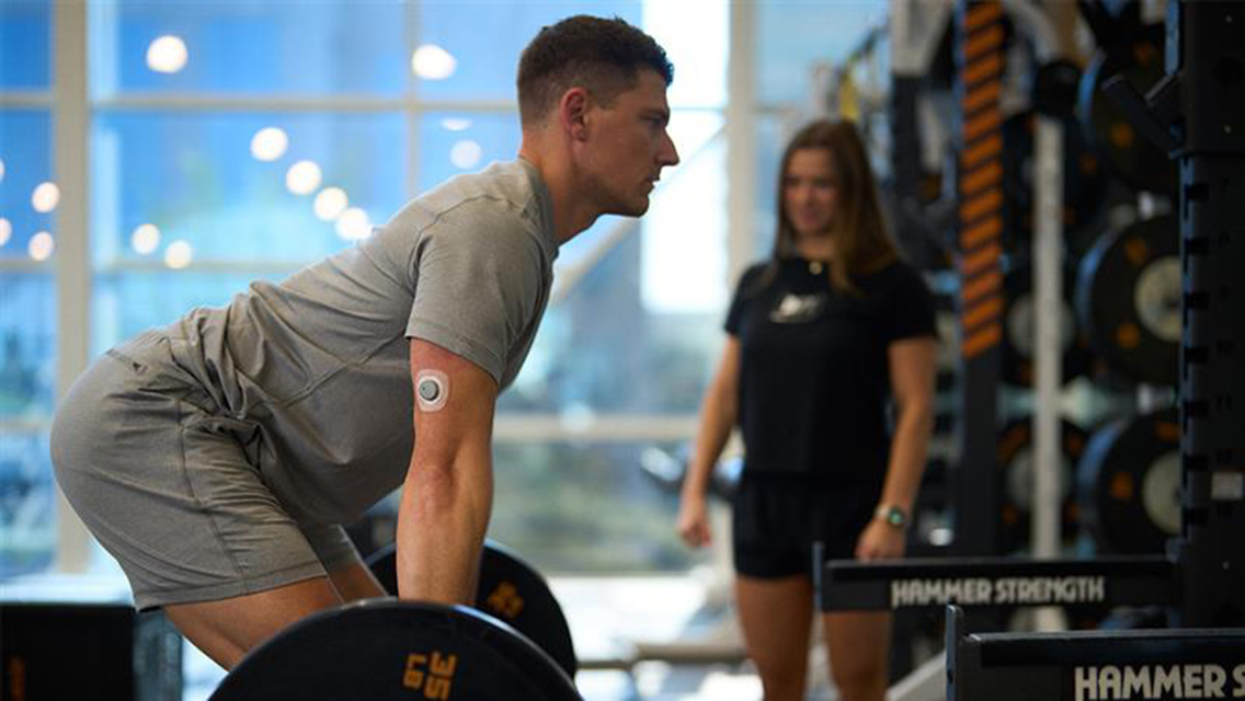 a man wearing a glucose monitor lifts weights