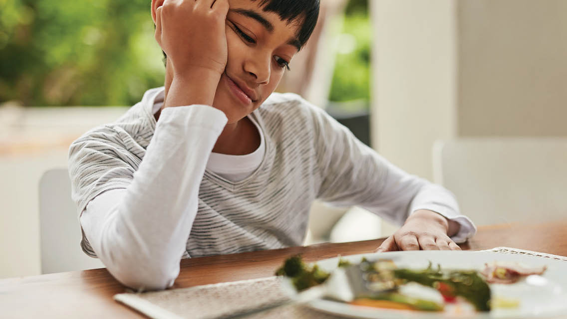 a young boy looks pessimistically at his dinner