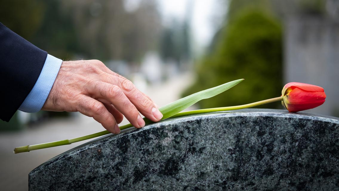 a person places a flower on a headstone