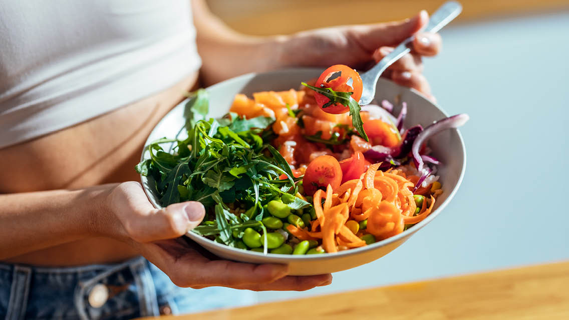 a woman eats a colorful bowl filled with plant-based foods