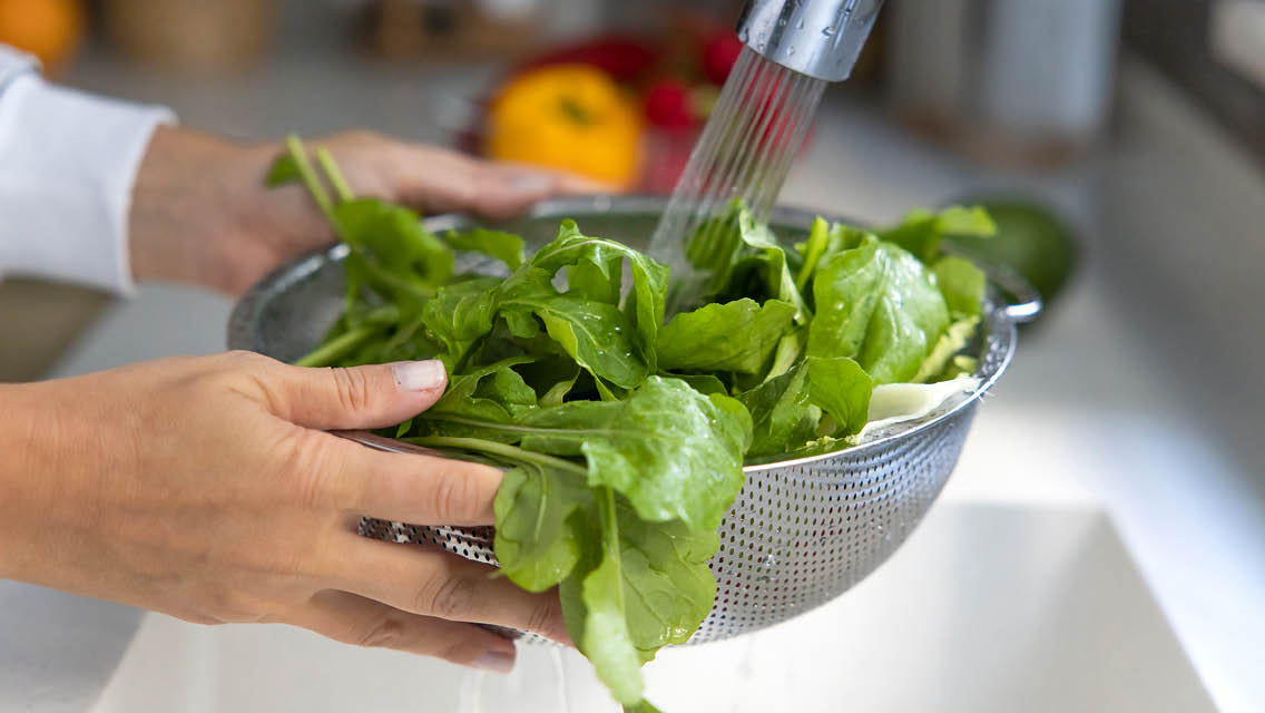 a person rinsing leafy greens