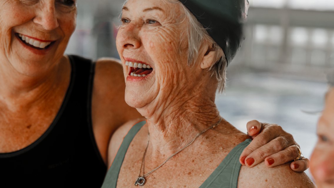 Two people wearing swim gear smiling near a pool