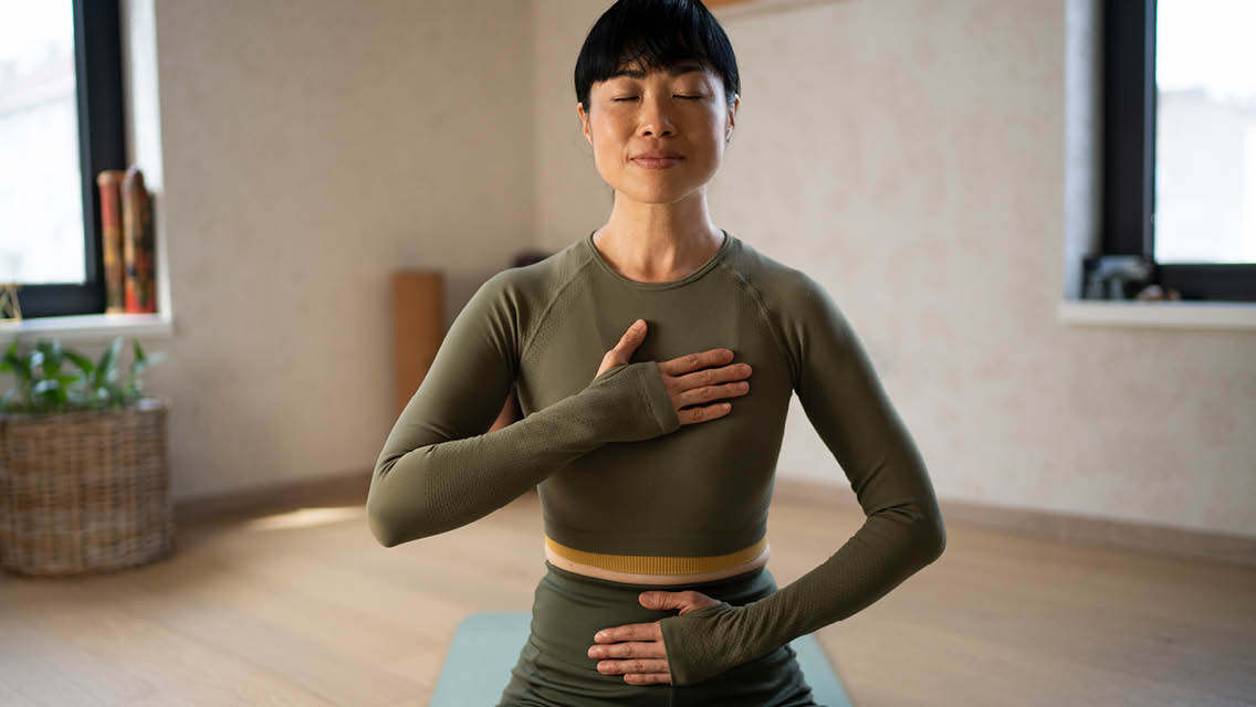 a woman breathes on her yoga mat with one hand on her heart and the other on her belly