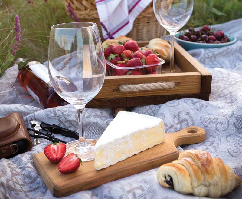 picnic scene with wine glasses, fruit, cheese, and bread