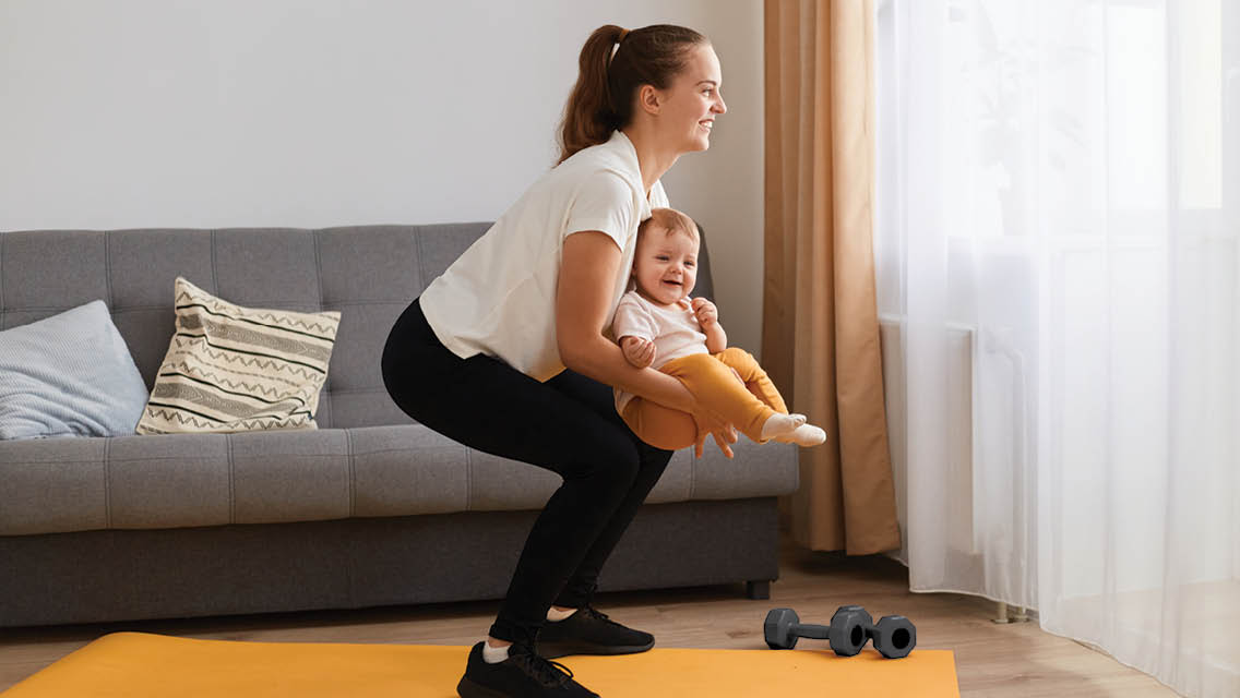 a woman performs a squat while holding her baby