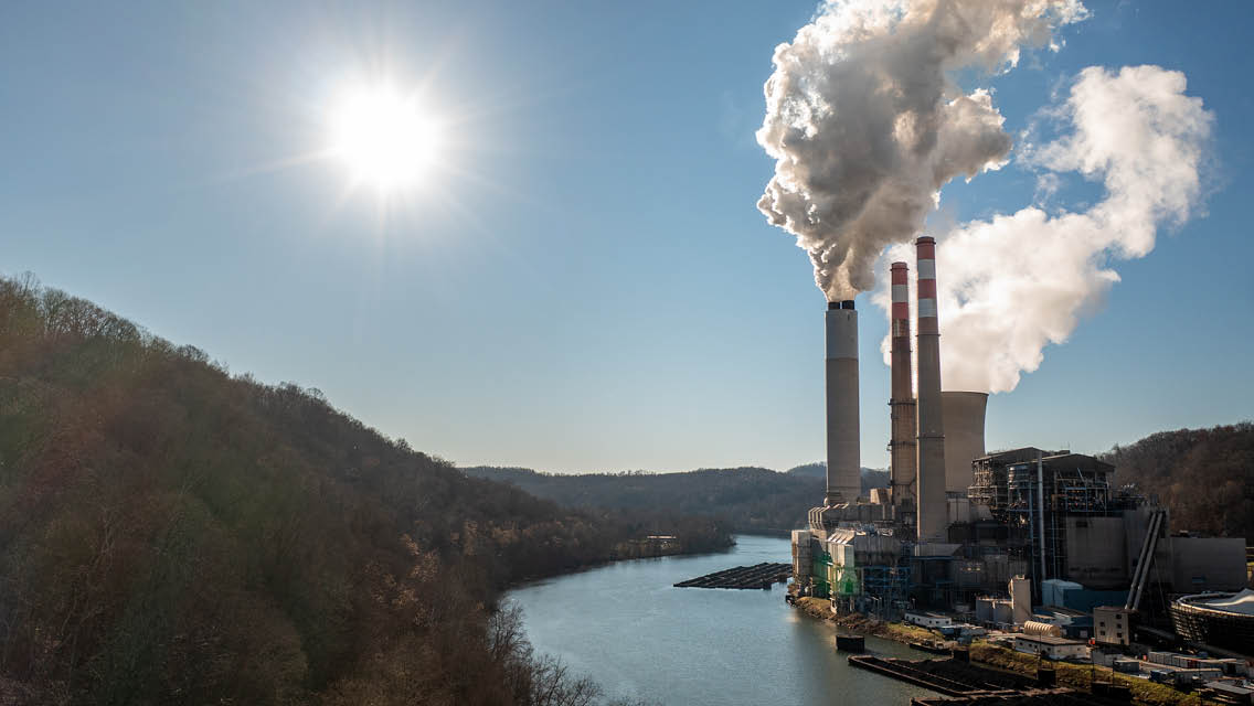 an energy plant spewing smoke by a river under a bright blue sky
