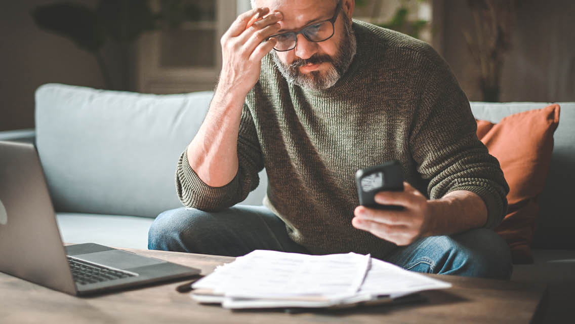 A stress-out man is doing paperwork and sitting in front of a laptop.