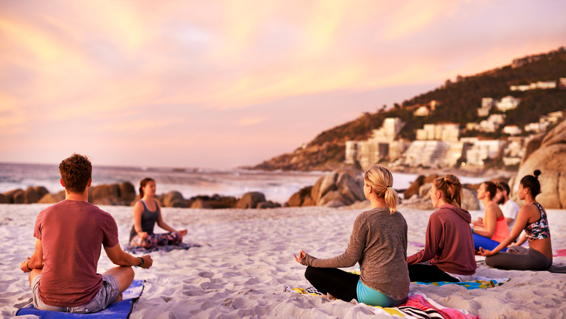 a yoga group sitting on a beach at sunset