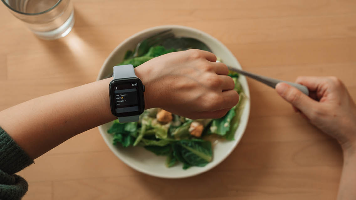 a person looks at their smart watch while eating a salad