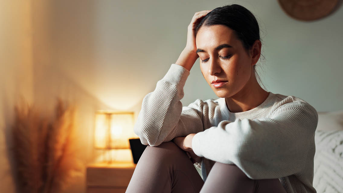 a woman sits on her bed with her head in her hand