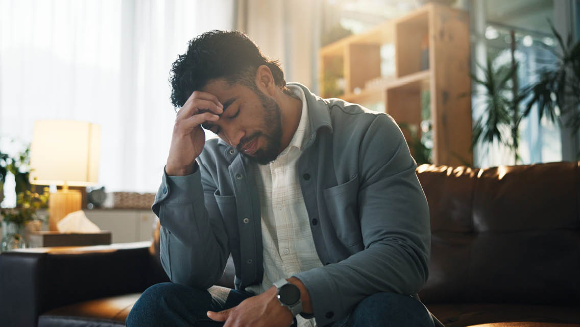 a man sits on his couch with his head in his hand