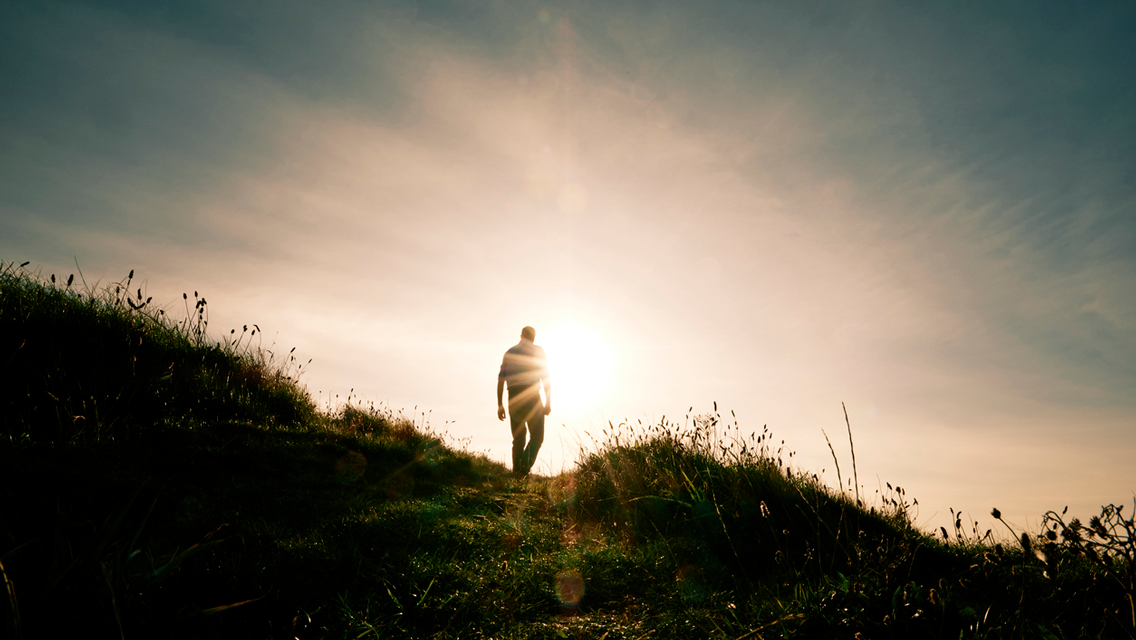 a person walking up a dark hill into the light