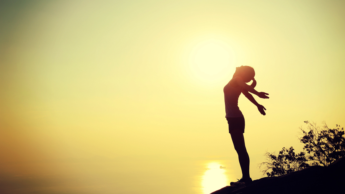 woman standing with arms stretched back at sunset