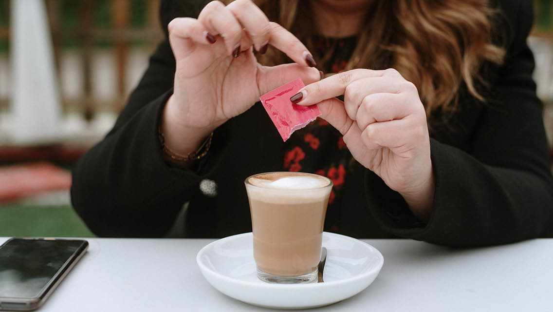 a person pours sweetener into her drink