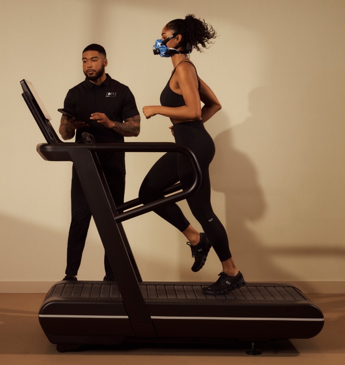 A woman going through an Active Metabolic Assessment at Life Time on a treadmill with a Dynamic Personal Trainer evaluating her results next to her.