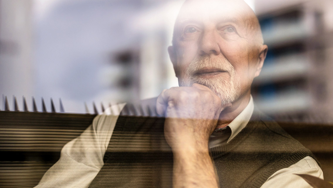 a senior man looks out a window