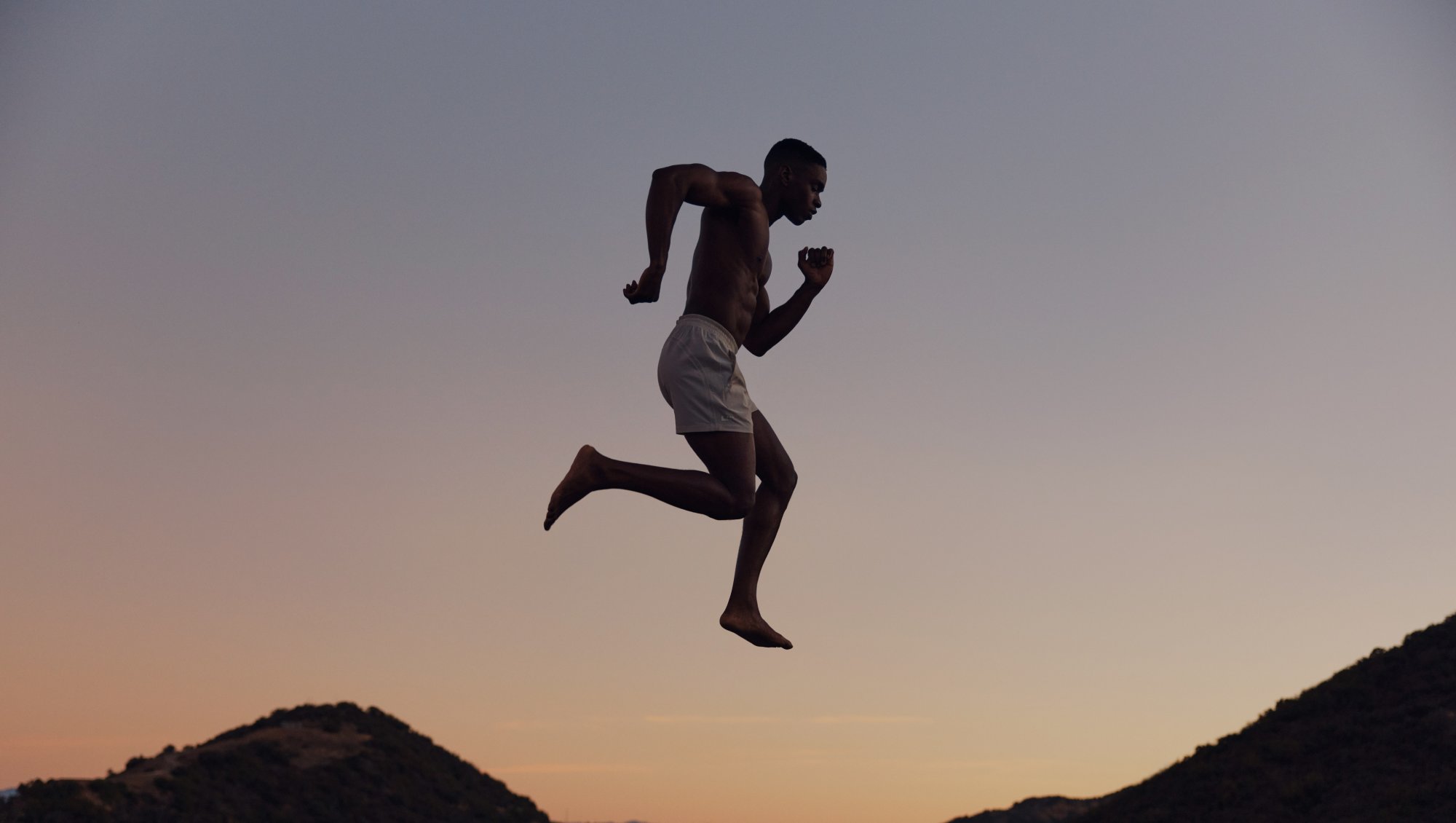 A man mid-jump over a beach during sunset.