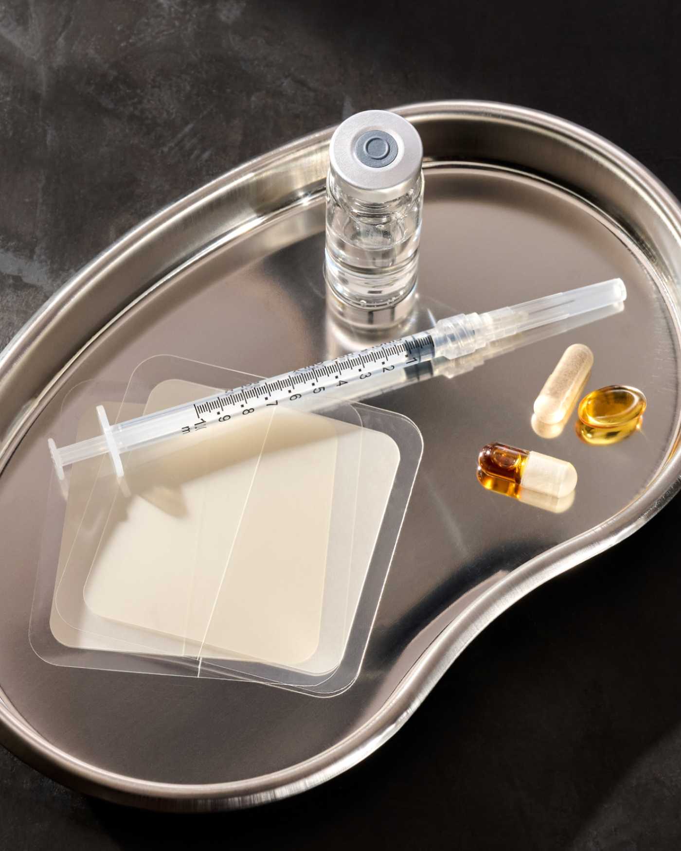 A silver tray with an injectable, hormone patch, and some supplements on it.