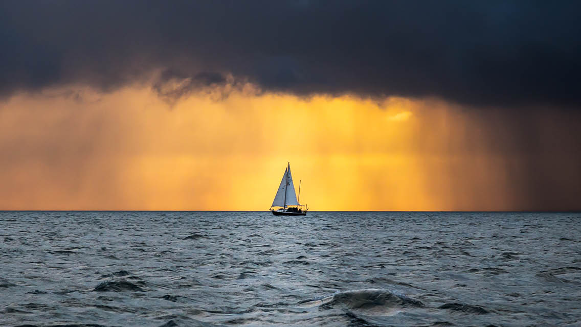 a sailboat at sunset in a sudden downpour