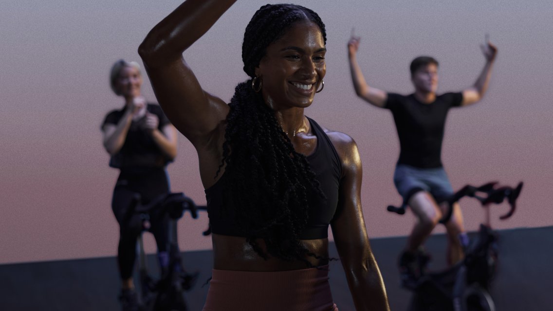 Woman on a stationary bike in a cycling class smiling with her arm in the air.
