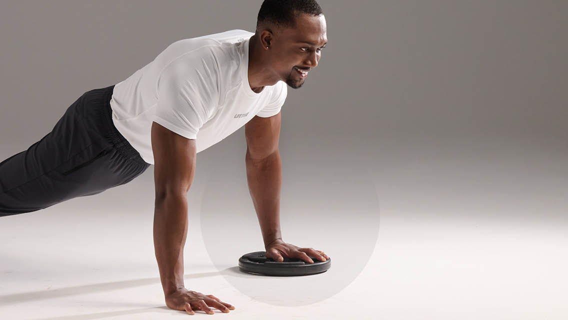 a man holds a push up position with a weight plate under one hand
