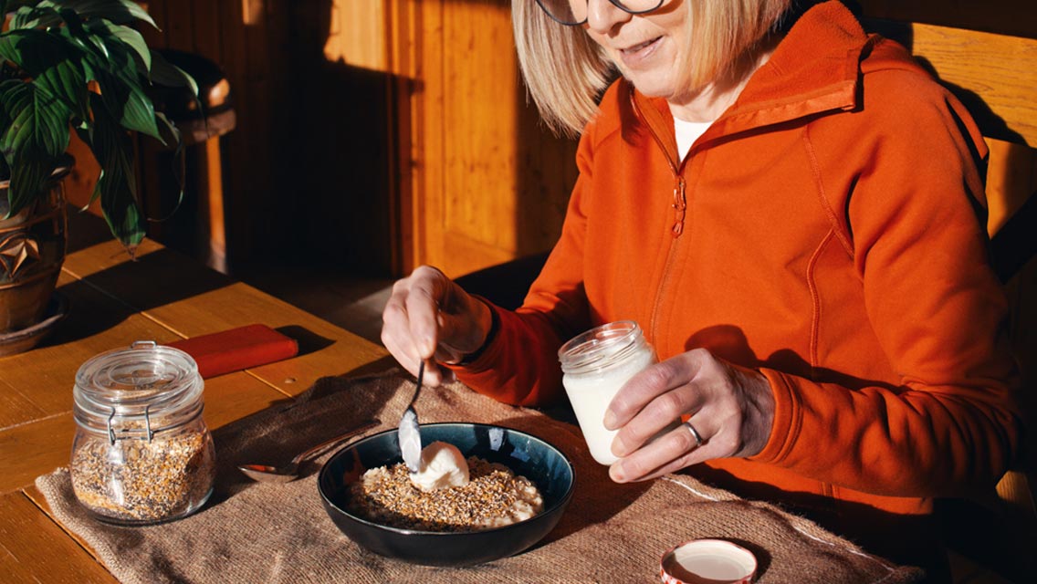 a woman scoops yogurt into a bowl of oats