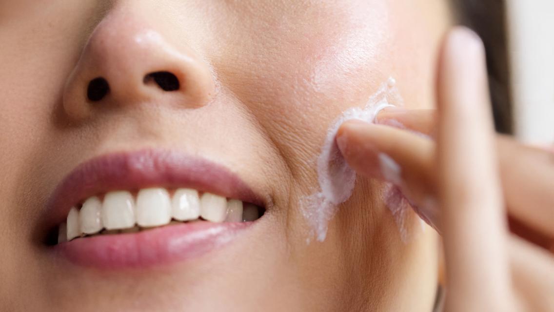 Woman putting lotion on her face.
