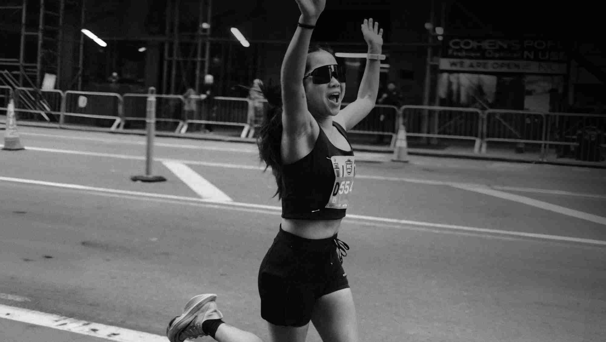 Woman running a race with her arms in the air celebrating.