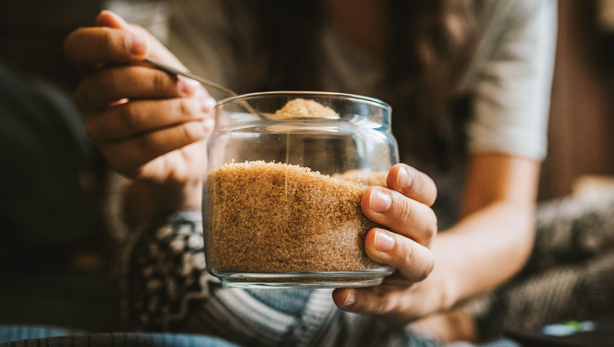 a person scooping brown sugar from a glass jar