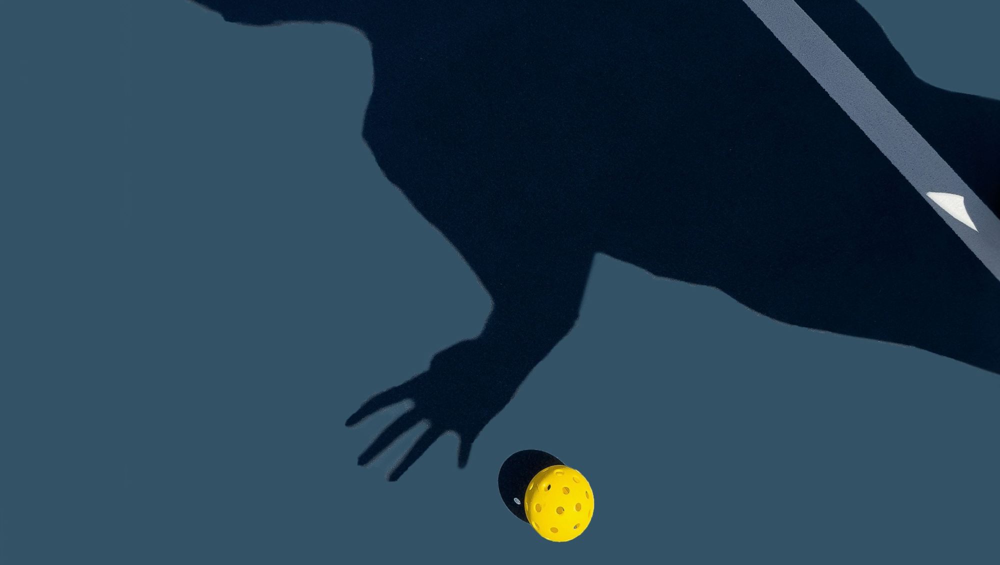 Shadow of a hand over a pickleball on a court.