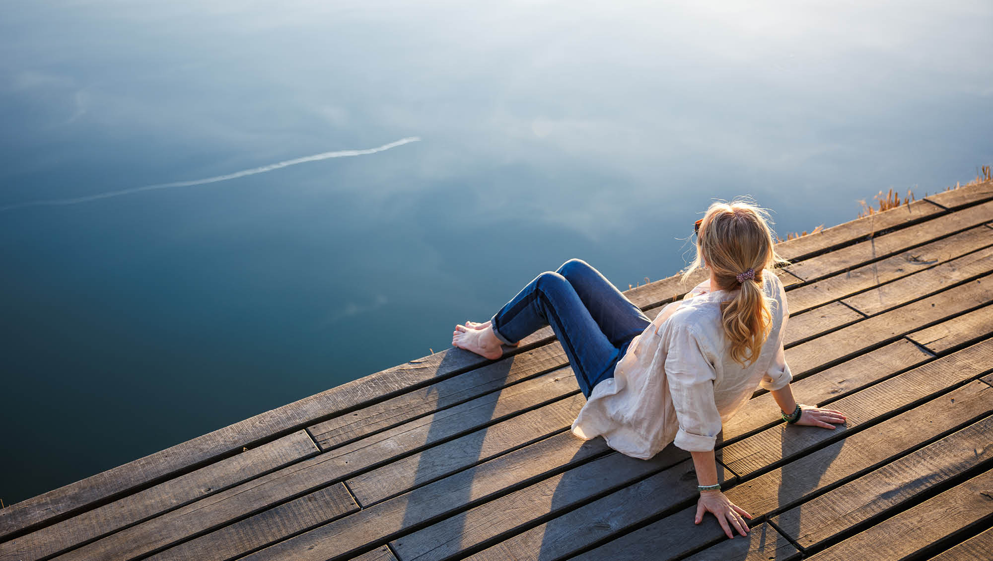 a woman sits on a dock looking at a lake