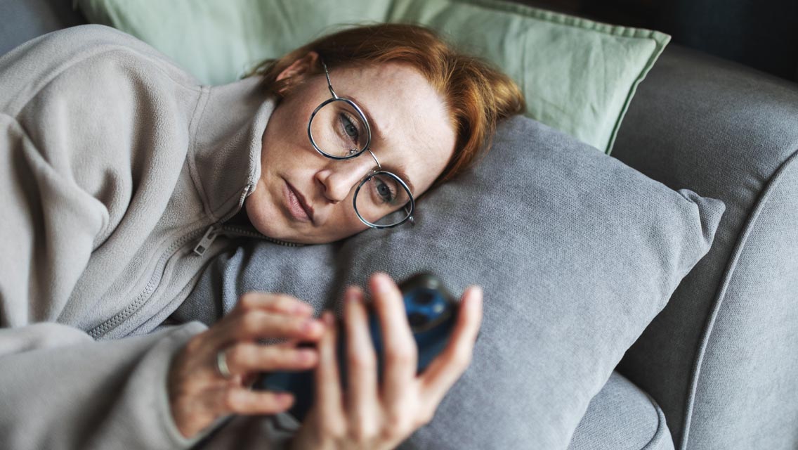 a woman lies on her couch looking at her phone