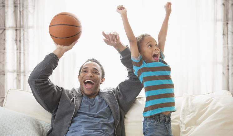 Mixed race father and son cheering with basketball on sofa