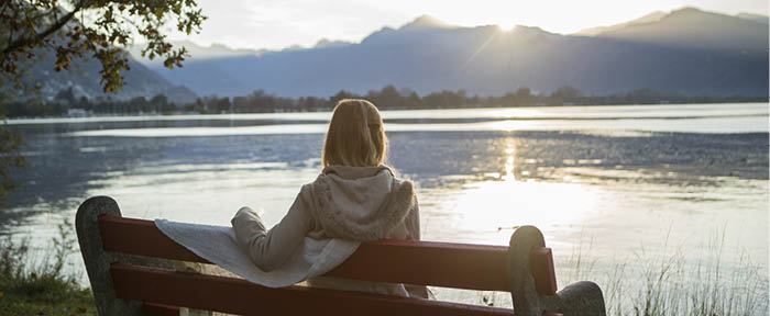 Woman sitting on bench with blanket watching sunrise